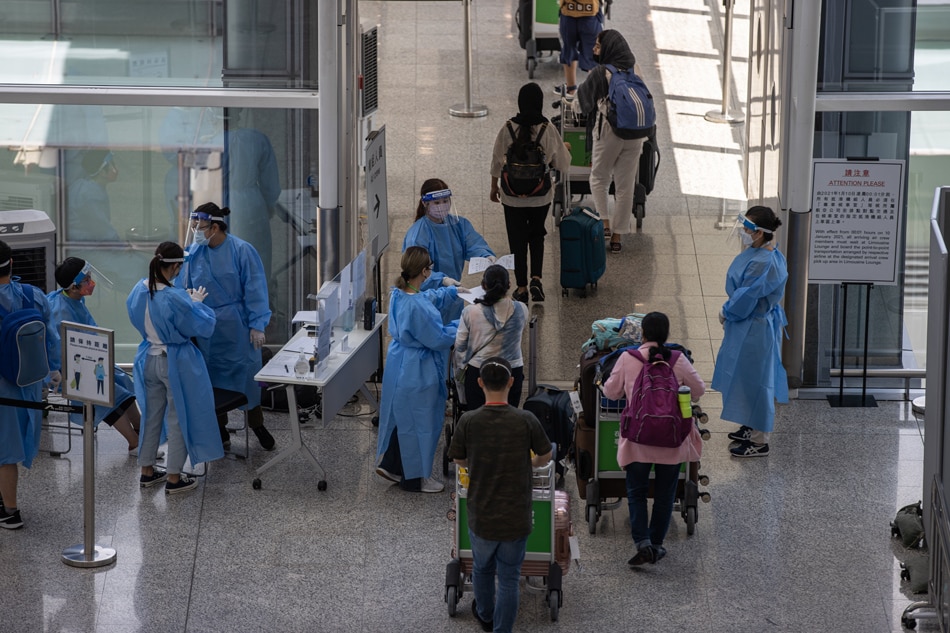 Health workers in protective gowns direct travelers to transportation to their quarantine hotel in the arrival hall at Hong Kong International Airport in Hong Kong, China, July 12, 2022. Jerome Favre, EPA-EFE/file