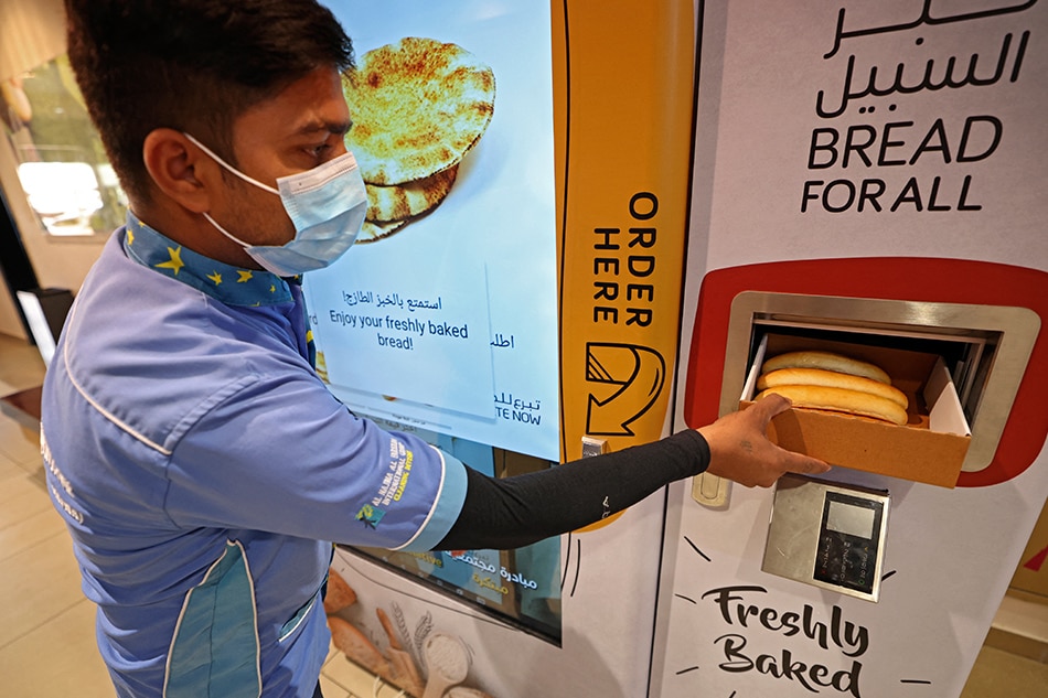 A man collects items from a vending machine that gives out free bread, in Dubai, on September 22, 2022. With the cost of living surging, free hot bread distributors for the poor have been introduced in Dubai, a rich Gulf emirate where millionaires living lavish lifestyles rub shoulders with hard-working migrants. Karim Sahib, AFP