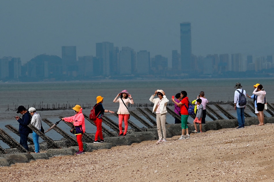 This photo taken on October 20, 2020 shows tourists posing for photos next to anti-landing spikes placed along the coast of Taiwan's Kinmen islands, which lie just 3.2 kms from the mainland China coast (in background) in the Taiwan Strait. The tank traps on the beaches of Kinmen Island are a stark reminder that Taiwan lives under the constant threat of a Chinese invasion – and fears of a conflict breaking out are now at their highest in decades. Sam Yeh, AFP/file