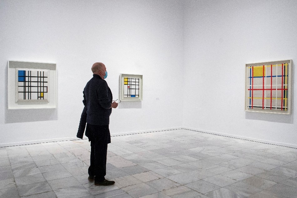 A visitor looks at the works (L-R) titled 'Rhythm of Black Lines (1937-1942)', 'Picture II with Red, Yellow and Blue (1936-43)' and 'New York City, 3 (unfinished) 1941' by Dutch artist Piet Mondrian displayed at the exhibition 'Mondrian and De Stijl' at the Reina Sofia Museum in Madrid, Spain, 10 November 2020. EPA-EFE/Luca Piergiovanni