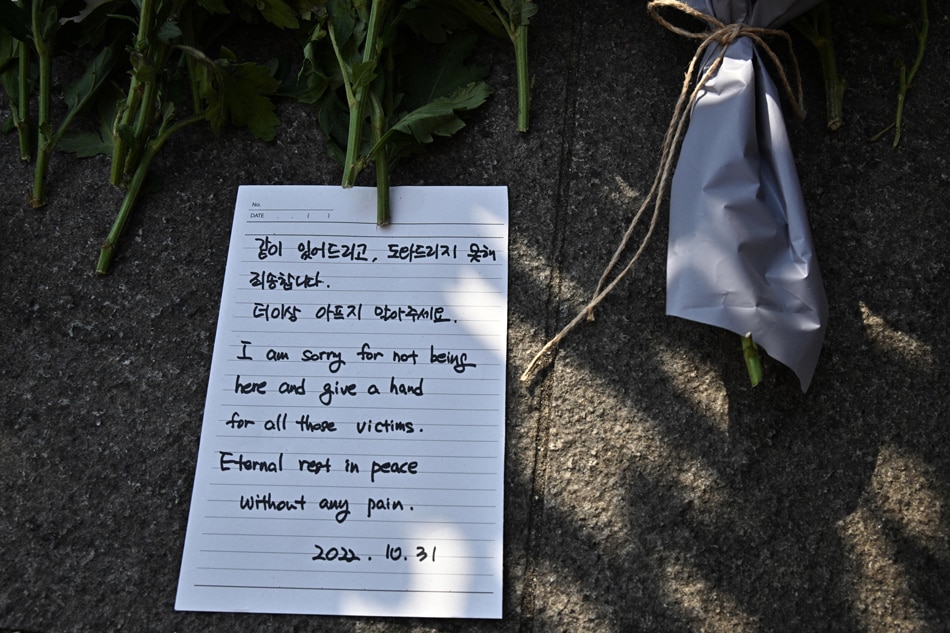 A handwritten note is left among flowers in tribute to those who were killed at a makeshift memorial outside a subway station in the district of Itaewon in Seoul on October 31, 2022, two days after a Halloween stampede in the area. Anthony Wallace, AFP