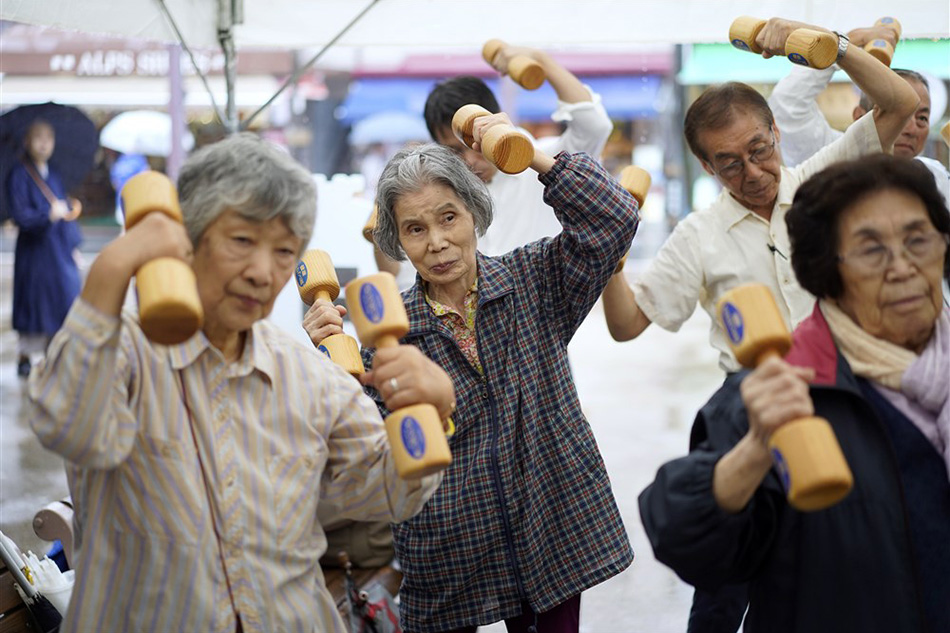 Elderly people practice physical activity with wooden dumbbells during an event marking the 