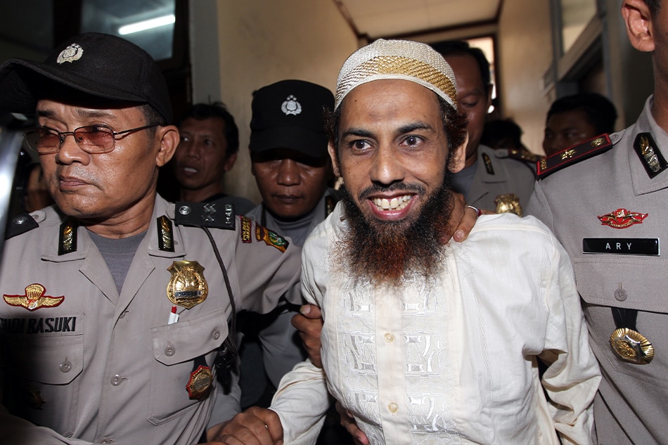 Indonesian terrorist Umar Patek (R) smiles as he was escorted by Indonesian Police officers during his Filipina wife, 29 year old Rokiah alias Fatimah Zahra's trial in Jakarta, Indonesia on 28 November 2011. Patek's wife Rokiah is on trial for using a false identity in 2009 to obtain an Indonesian passport, which she used to travel to Pakistan. Prosecutors say Ruqayyah, a national of the Philippines, illegally applied for an Indonesian passport using a false name and date and place of birth. EPA/BAGUS INDAHONO/FILE