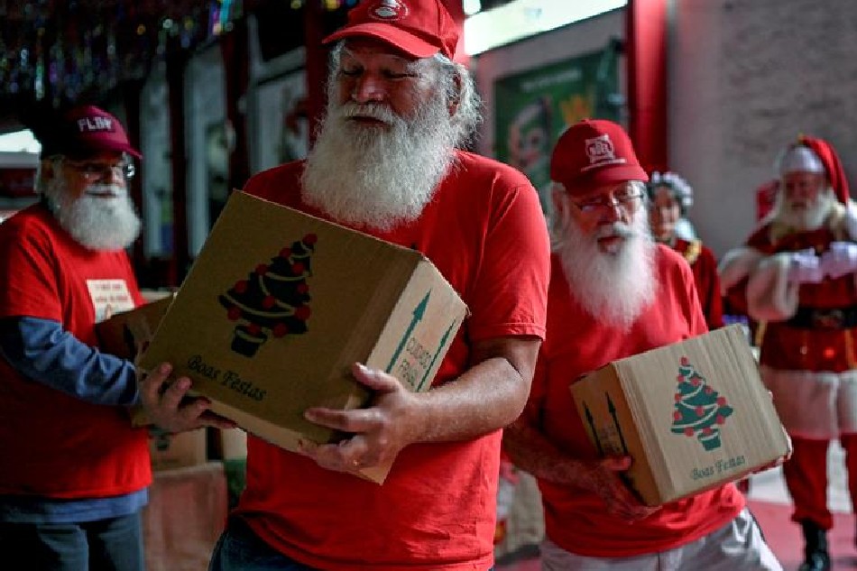 A group of professional Santa Claus carry Christmas food baskets they received during a charity event organized by Brazil's School of Santa Claus and a food distribution company, at the Estacio de Sa Samba School barrack in Rio de Janeiro, Brazil, on December 20, 2022. The donation of Christmas baskets to professional Santa Claus and Mrs. Claus started during the COVID-19 pandemic as a way to aid this working class, severely hit during that time. MAURO PIMENTEL / AFP