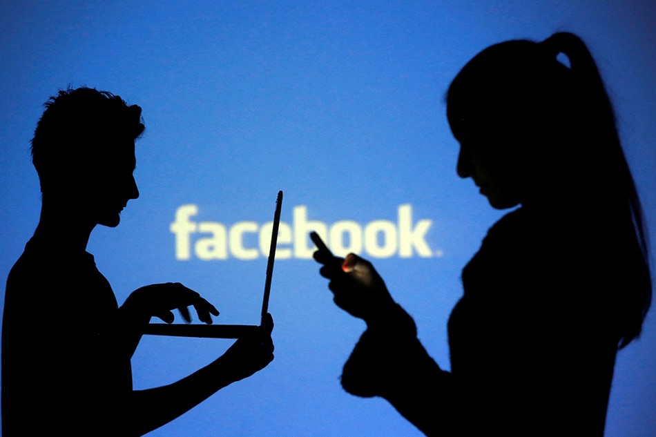 People are silhouetted as they pose with laptops in front of a screen projected with a Facebook logo, in this picture illustration taken in Zenica October 29, 2014. REUTERS/Dado Ruvic/File Photo