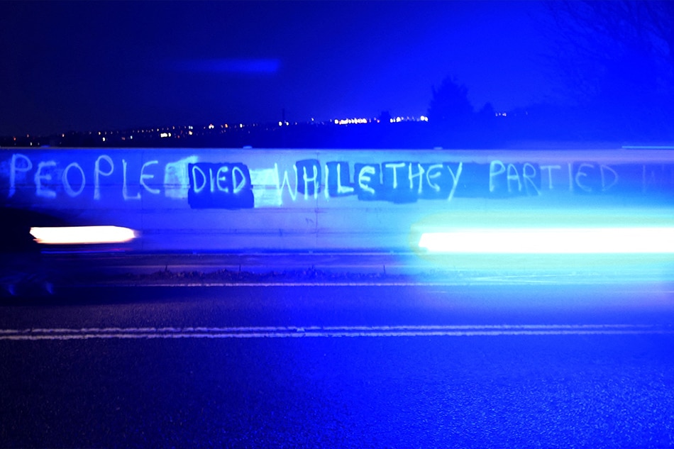 A police car drives past graffiti on a pedestrian bridge saying 
