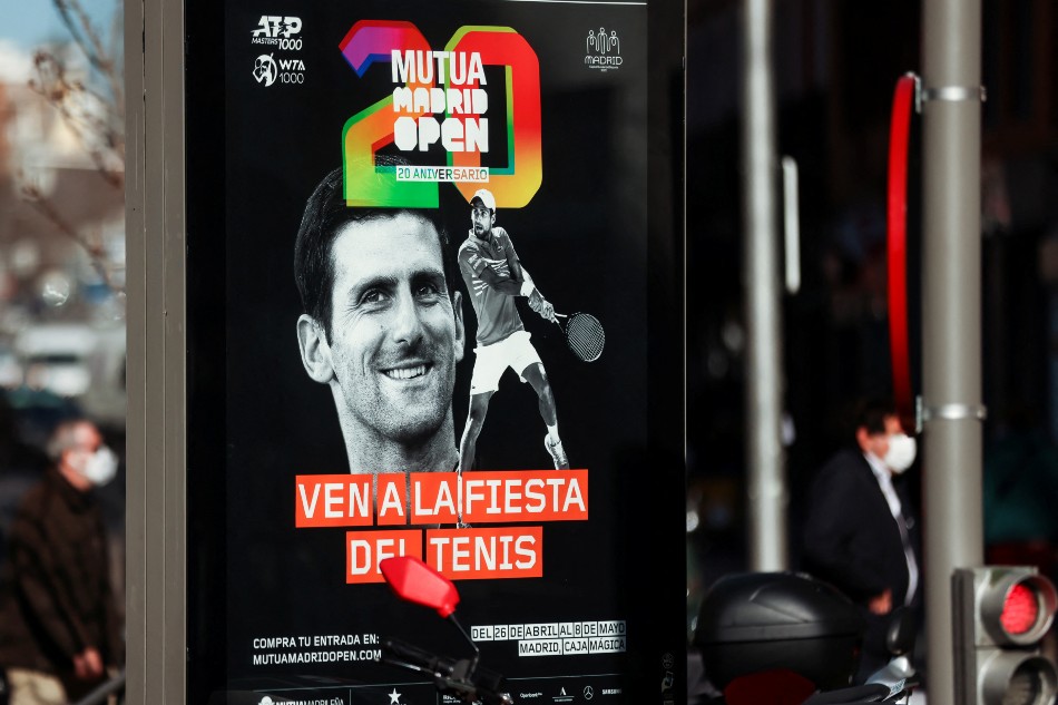 People wearing protective face masks walk past a poster with the image of tennis player Novak Djokovic announcing the Madrid Open, in Madrid, Spain January 18, 2022. Nacho Doce, Reuters.