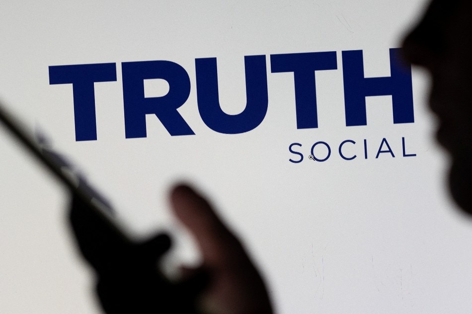 The Truth social network logo is seen displayed behind a woman holding a smartphone in this picture illustration taken February 21, 2022. Dado Ruvic, Reuters/Illustration