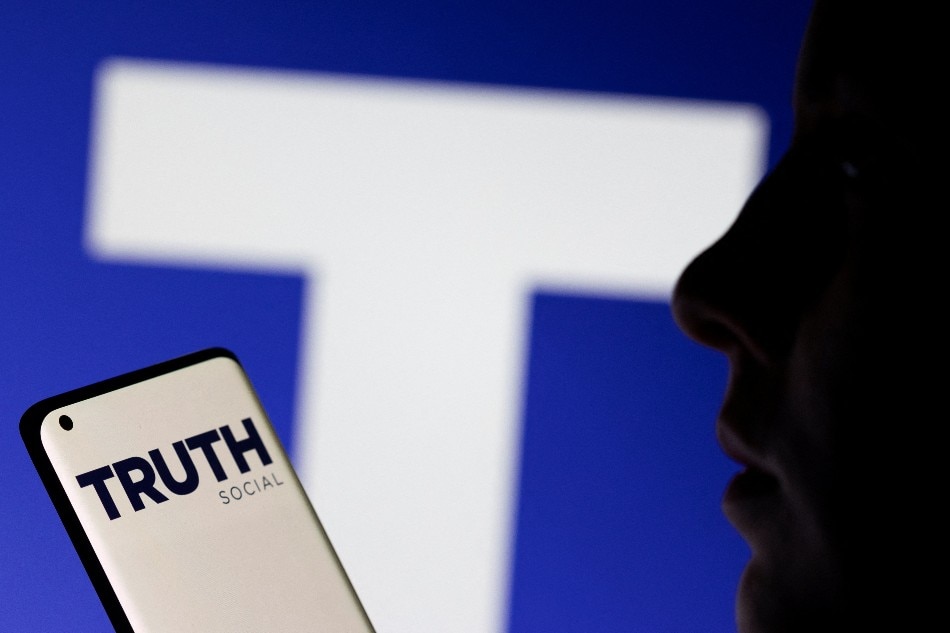 The Truth social network logo is seen displayed behind a woman holding a smartphone in this picture illustration taken February 21, 2022. Dado Ruvic, Reuters/Illustration