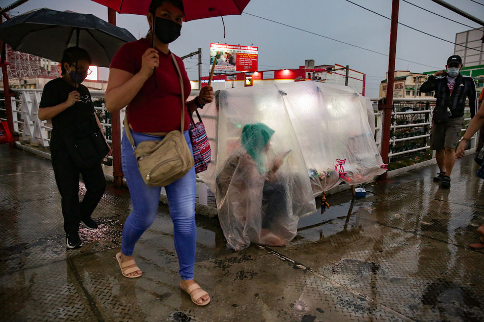 A sidewalk vendor protects herself from the rain using a plastic cover at a footbridge in Pasay City on May 17, 2022. George Calvelo, ABS-CBN News 