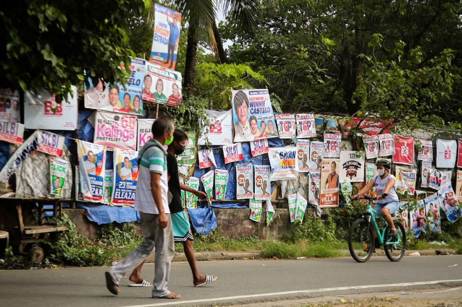 People walk past posters of candidates during the campaign season for the national and local elections on March 28, 2022 at Barangay Bliss in Quezon City. Jonathan Cellona, ABS-CBN News