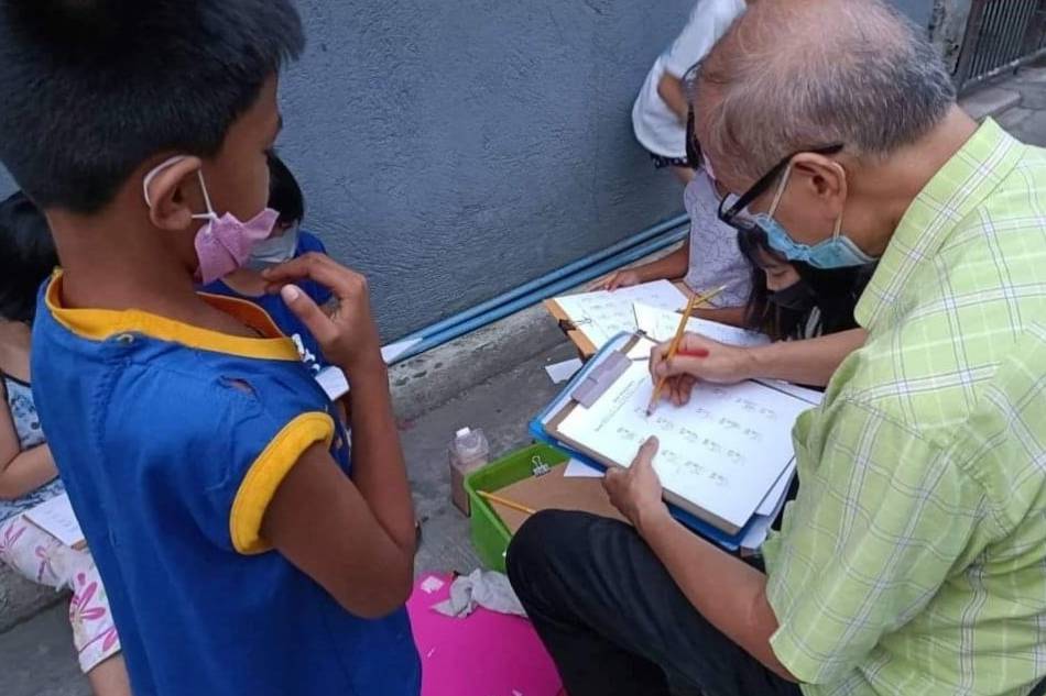 Several children gather around retired teacher Delfin Angeles as he helps them with their school lessons. Photo courtesy of his daughter Carmela Angeles 