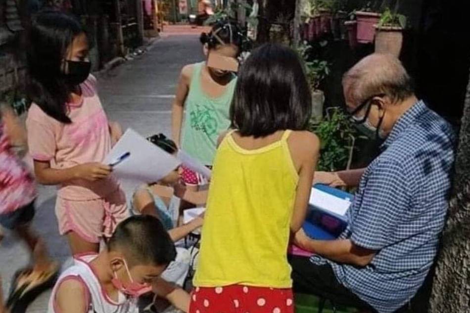 A group of children review their lessons with the help of retired teacher Delfin Angeles outside his home. Photo courtesy of Carmela Angeles