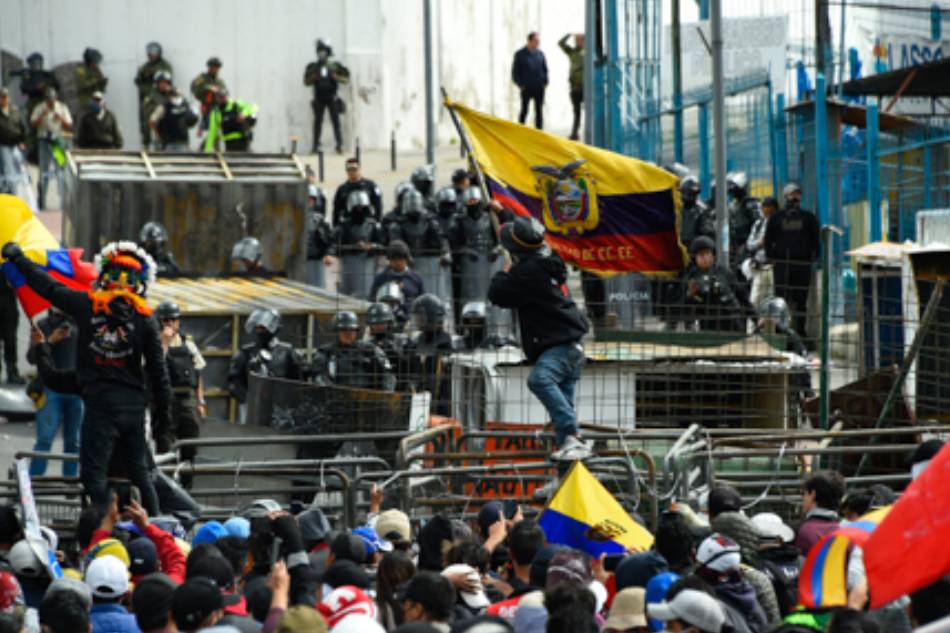 A demonstrator waves an Ecuadorean national flag while police officers stand guard in the surroundings of the National Assembly in Quito on June 25, 2022, when a parliamentary session called by opposition lawmakers for a no confidence vote against President Guillermo Lasso will be held in the framework of indigenous-led protests against the government. Rodrigo Buedia, AFP