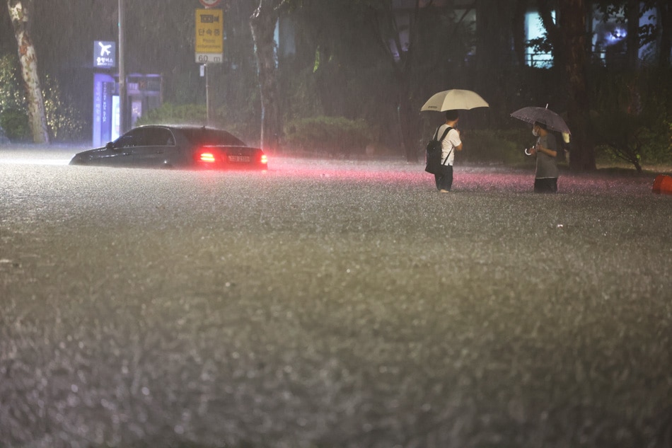 People wade alongside submerged cars in a street during heavy rainfall in the Gangnam district of Seoul on Monday. Record heavy rains caused massive flooding in South Korea’s central region forcing suspension of subway lines operation and evacuation of residents in low-lying areas. YONHAP/AFP