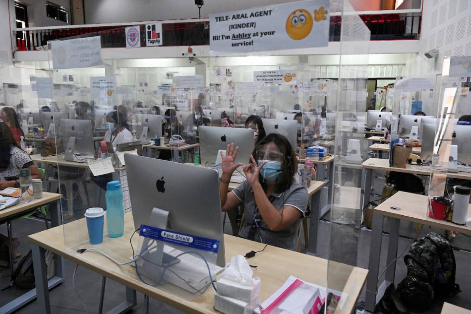 A registered teacher wearing a face mask and shield as a precaution against COVID-19 gestures in front of a computer as she and dozens other teachers conduct a teleconference with struggling students, helping them in their school lessons at a local government-sanctioned online tutorial class in Taguig City on March 3,2021. Ted Aljibe, AFP