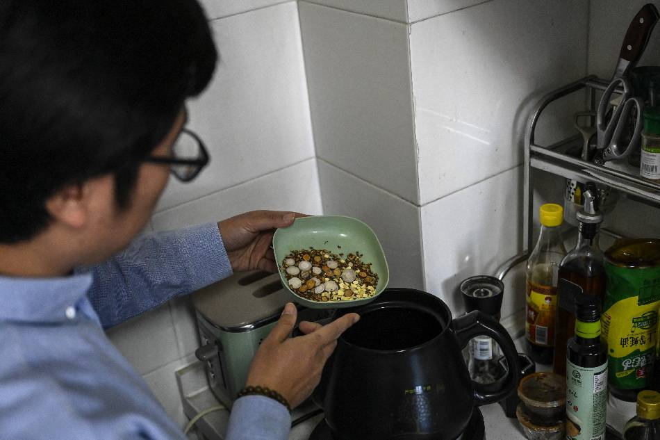 The photo taken on December 23, 2022 shows a Chinese medicine enthusiast Mex Yu pouring a plate of traditional herb medicine into a pot at his home in Beijing. As Covid-19 rips through China's vast population, making millions sick and fuelling a shortage of drugs, many are turning to old-school traditional medicines to battle the aches and pains of the virus. Jade Gao / AFP