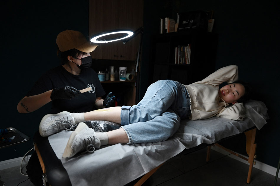  This photo taken on February 27, 2023 shows Chinese tattoo artist Song Jiayin tattooing the leg of her client Liao Jingyi at her studio in Beijing. For over two years, Song has interviewed her female clients and posted the results online, recording the memories, hopes and fears of hundreds of women in ink and video. Greg Baker, AFP