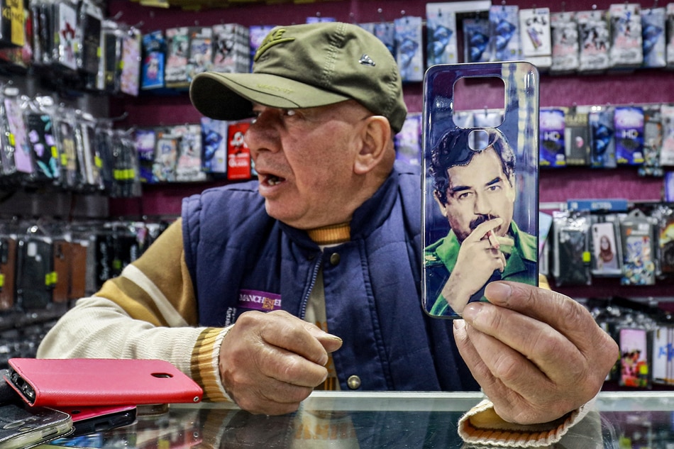 In this picture taken on April 5, 2023, Shaher Abu Sharkh, a 67-year-old Jordanian mobile phone accessory merchant holds up a cell phone cover showing the image of Iraq's late ousted dictator Saddam Hussein in his shop in Amman. Photo by Khalil Mazraawi, AFP