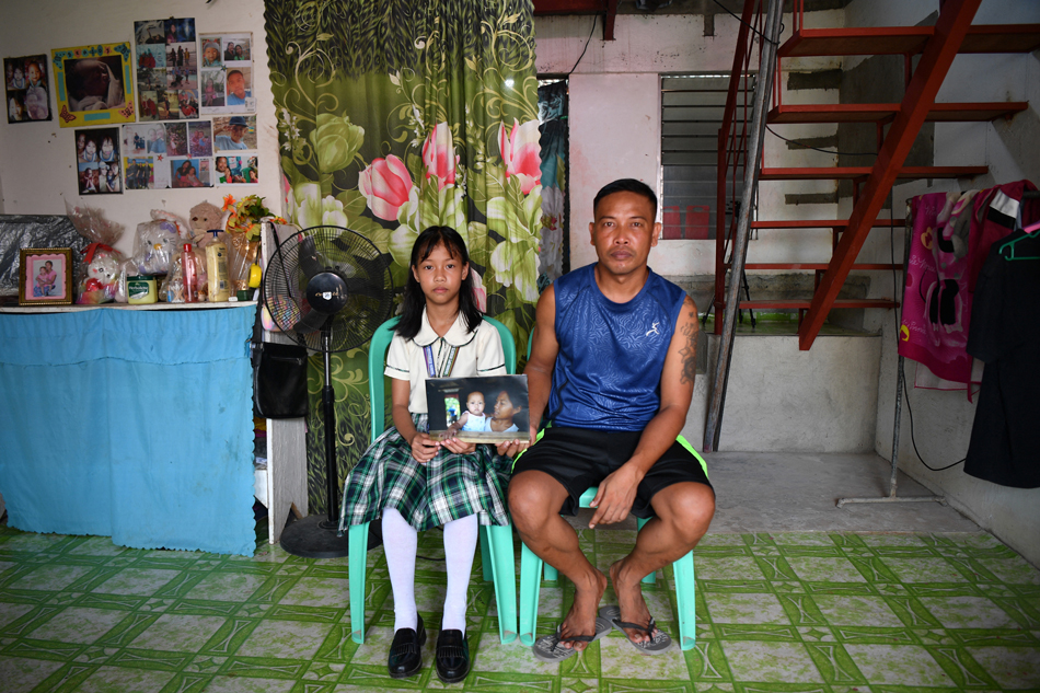 This photo taken on October 10, 2023 shows Bea Joy Sagales (L) holding a photo of herself as a baby with her mother Emily who now works as a domestic helper in Saudi Arabia, as she poses with her father Jobert in their residence at a resettlement village in Tacloban city, Leyte province. Bea Joy