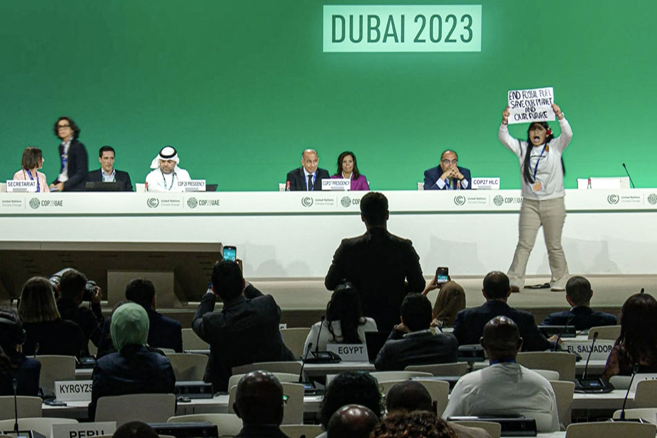 This image grab taken from AFPTV video footage shows an activist protesting on stage against fossil fuels during an event at the United Nations Climate Conference (COP28) in Dubai on December 11, 2023. A new draft climate agreement proposed on December 11 by the Emirati presidency of UN COP28 talks called for reducing the production and consumption of fossil fuels but it no longer mentioned a 