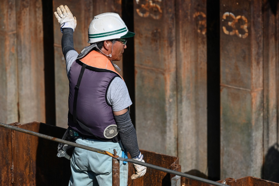 This photo taken on August 4, 2023 shows a man wearing a vest with battery-powered built-in fans, along with cooling sleeves over his arms, to keep cool in the heat, while working along a river in Tokyo. Richard A. Brooks, AFP