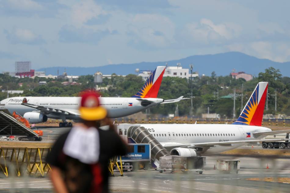 A Philippine Airlines plane is seen in the background as a man uses his phone at the arrival area of the Ninoy Aquino International Airport (NAIA) Terminal 1 in Pasay City on May 24, 2021. Jonathan Cellona, ABS-CBN News
