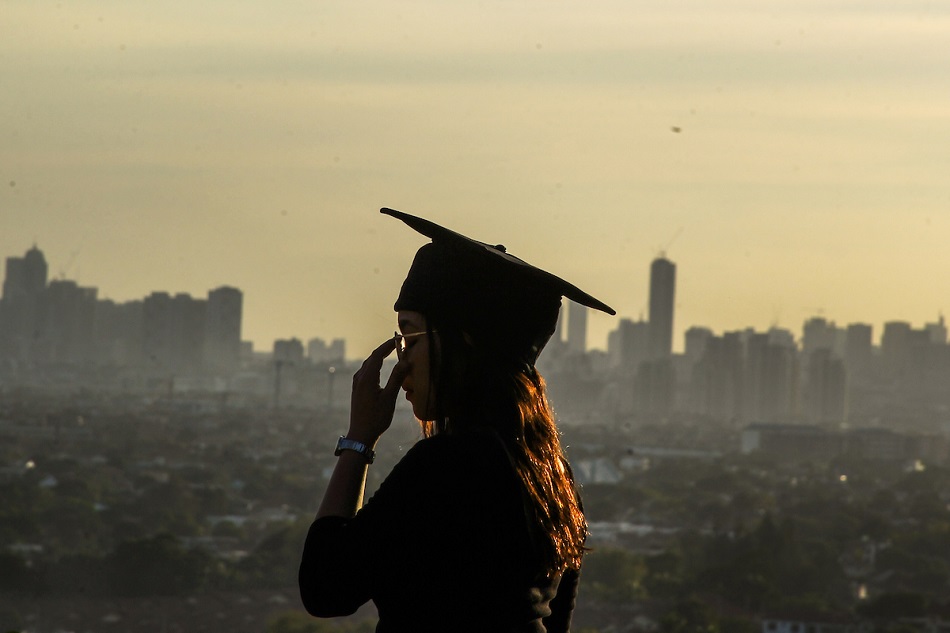 A young woman, set for graduation, poses for a photo with the city scape in the background as seen from Antipolo City, March 19, 2019. Jonathan Cellona, ABS-CBN News/File