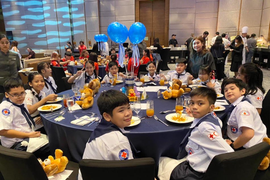 Photo caption: Micot Juico, food coordinator of the Red Cross Philippines, with their student beneficiaries from Villamor Air Base Elementary School