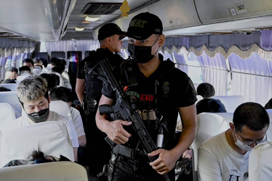Policeman secure Chinese nationals on a bus ahead of their deportation after they were detained in a raid on a suspected sex trafficking and online scam operation in Pasay, Metro Manila, on Dec. 14, 2023. Chinese, Korean, Vietnamese and Filipino nationals were among the nearly 600 people found inside a compound during the operation in October. Jam Sta. Rosa, AFP 