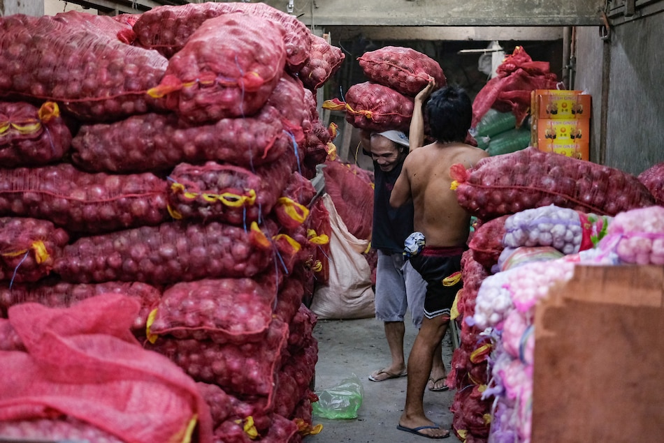 Workers unload bags of red onions inside a storage area in Divisoria market in Manila on Aug. 18, 2022. George Calvelo, ABS-CBN News/File