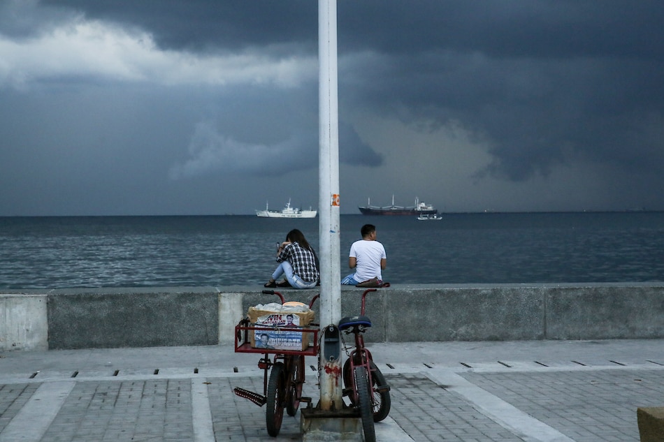 A couple sits along the breakwater on Manila Bay on Friday as storm clouds gather on the horizon. Jonathan Cellona, ABS-CBN News/File 