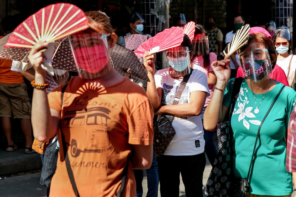 Filipino Catholics use fans to protect their face from the sun as they fall in line along Carriedo Street hoping to get inside the Quiapo Church on March 26, 2021. George Calvelo, ABS-CBN News/File