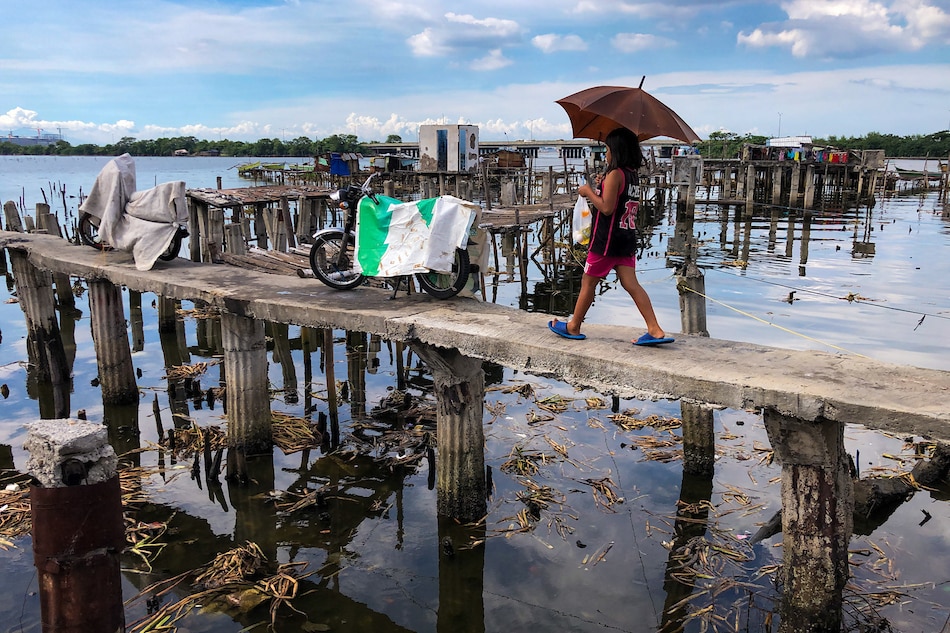 A woman walks on a narrow bridge towards huts made out of light materials at a fishing community in Bacoor, Cavite on October 30, 2020. George Calvelo, ABS-CBN News 