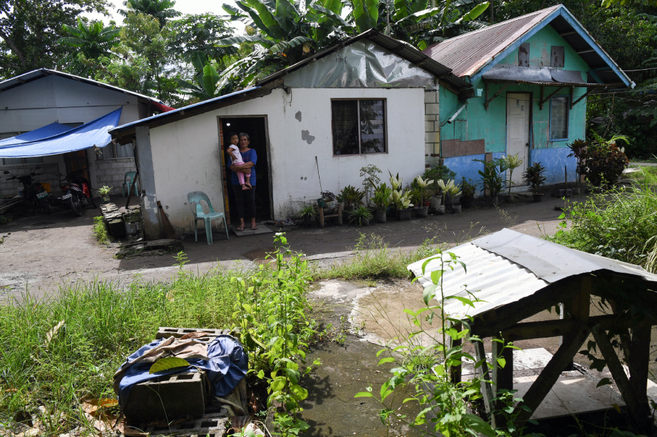 This photo taken on October 11, 2023, Super Typhoon Haiyan survivor Agatha Ando cuddling her grandchild look at the tombstone with the remains of her husband, three of her seven siblings, and four nephews and nieces in front of their house in San Jose district of Tacloban City, Leyte province. Ten years after she buried her husband and seven of her kin at her front yard, Ando continues to live at ground zero of one of the Philippines