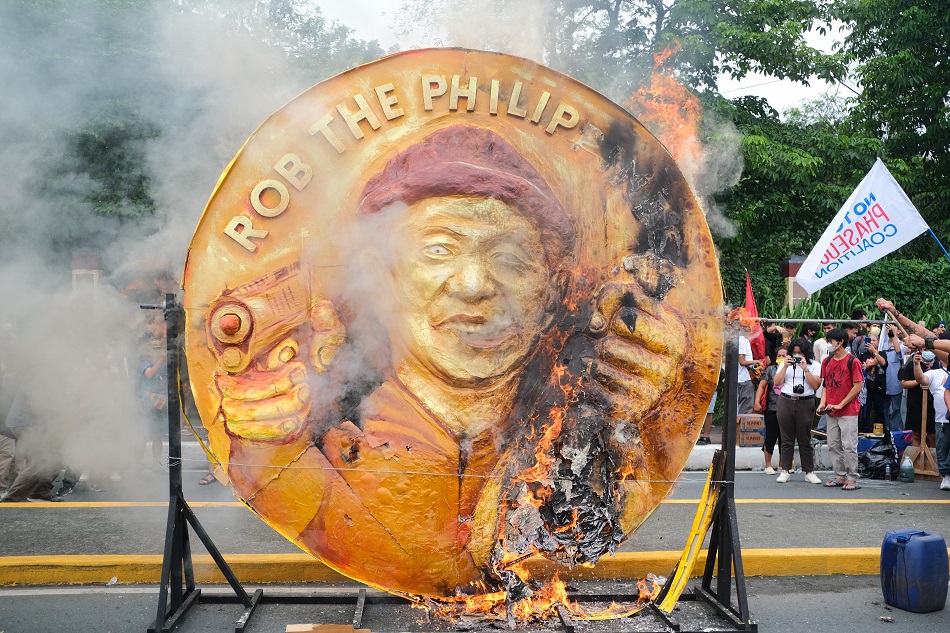 Anti-government protesters burn an effigy with the images of President Ferdinand Marcos Jr. on a two-faced coin symbolizing the meager wage increase for workers on one side and a smiling image on the other, projecting unity, peace, and love of the country, during a march on Commonwealth Avenue hours before the president is set to deliver his second State of the Nation Address on July 24, 2023. Alec Corpuz, ABS-CBN News