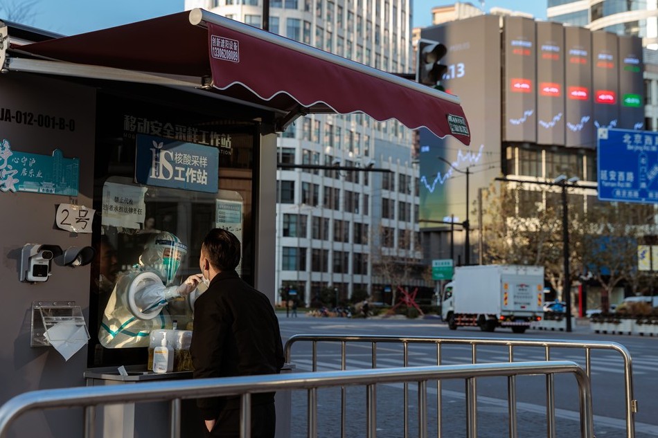 A man takes Coronavirus PCR test in the testing booth on the street in front of the large screen showing latest stock exchange data, in Shanghai, China, 03 January 2023. Photo by Alex Plavevski, EPA