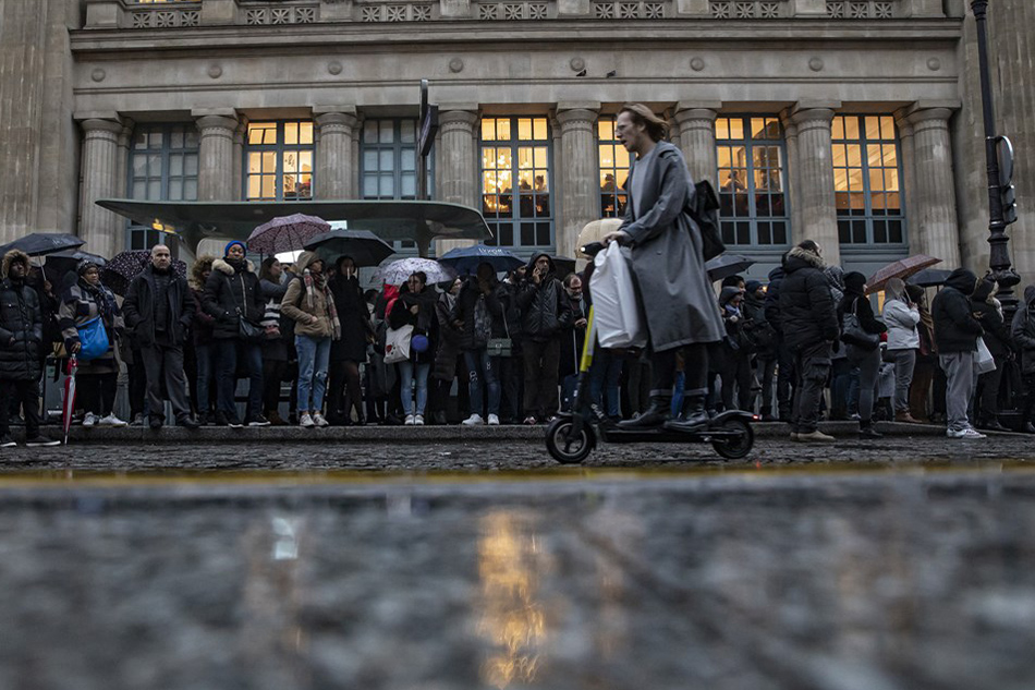 A woman rides an electric scooter (e-scooter) as commuters wait at a bus stop outside Gare du Nord train station during a general strike action, in Paris, France, 16 December 2019. EPA-EFE/IAN LANGSDON
