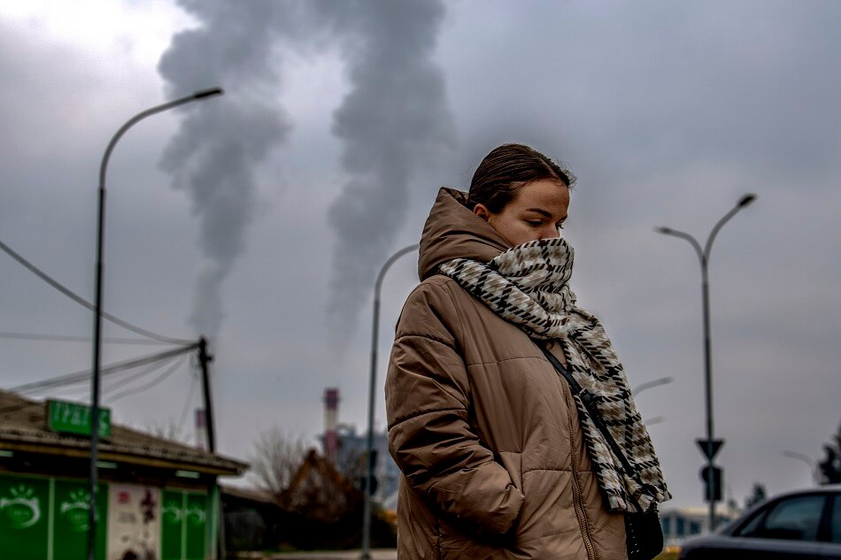 A girl wears a scarf over her face as she walks past a factory whose chimneys release smoke above the smog and pollution-covered capital Skopje, Republic of North Macedonia, 30 December 2022. Georgi Licovski, EPA-EFE/File