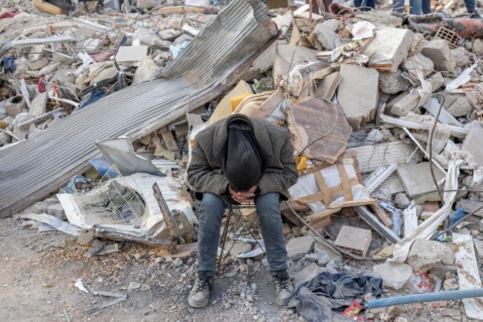 A man sits on the rubble of a collapsed building during rescue operations in Hatay on February 12, 2023, after a 7,8 magnitude earthquake struck the border region of Turkey and Syria earlier in the week. BULENT KILIC / AFP