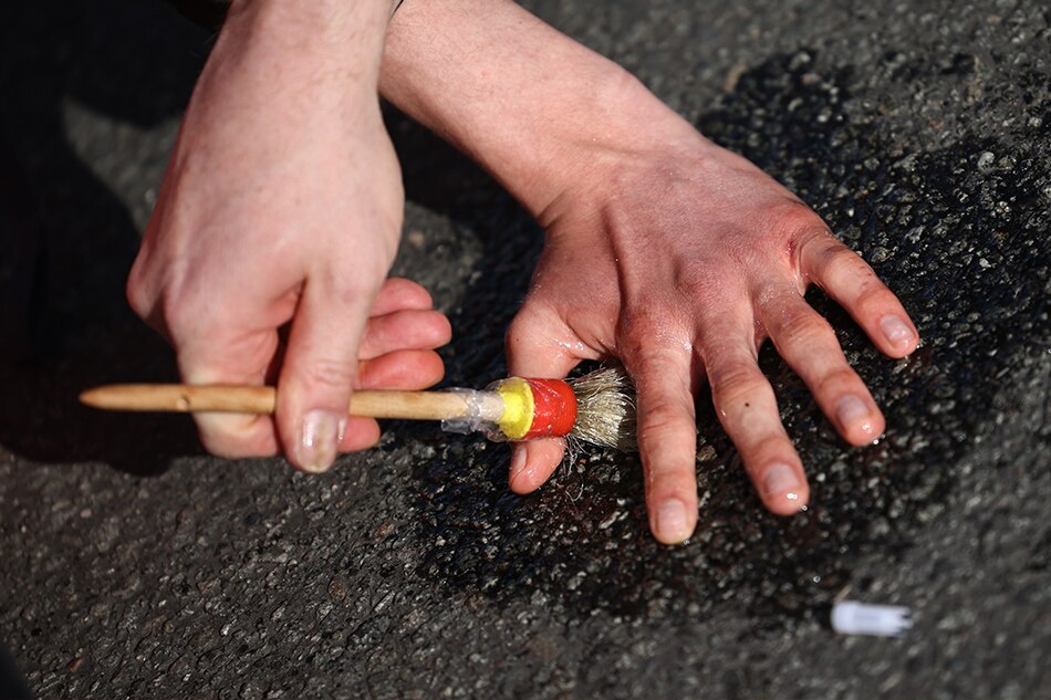 A police officer (L) applies solvent to an activist's hand glued to the ground while blocking a street during a climate protest at the victory column in Berlin, Germany, 24 April 2023. The climate protest organization Letzte Generation announced actions of civil disobedience taking place on 24 April 2023 as climate protests in Berlin. EPA-EFE/CLEMENS BILAN