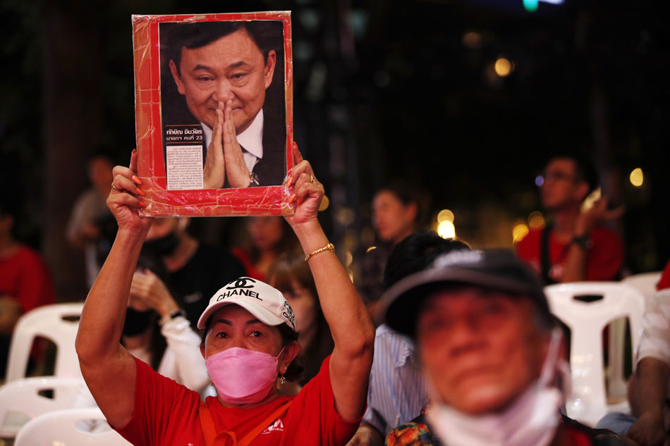 A supporter of Pheu Thai Party holds up a portrait of the former prime minister and founder of the party, Thaksin Shinawatra, while watching a television broadcast of the election vote counting after polls closed in the general election at the party