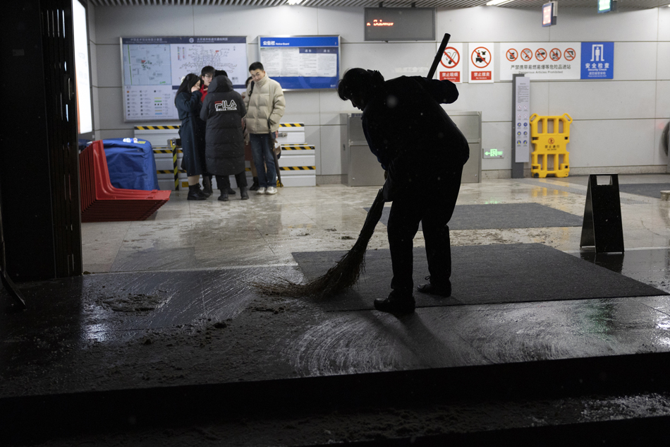 A woman clears the snow out of the entrance of a metro station with a broom in Beijing, China, Dec. 14, 2023. Andres Martinez Cacares, EPA-EFE 