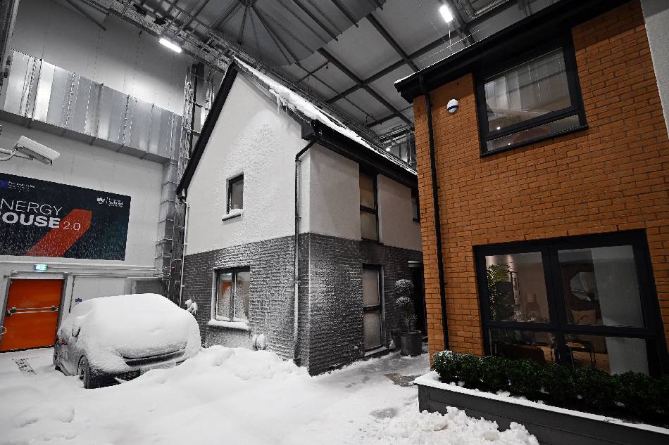 Simulated snow covers a car and the walls of one of two houses built to develop future heating solutions, at Energy House 2.0 at Salford University in Salford, north west England on January 24, 2023. A blizzard descends on two houses in northwestern England in a cutting-edge science experiment to save energy and help tackle climate change. The newly-built detached homes, equipped with zero-carbon technology to withstand extreme temperatures, sit in a cavernous laboratory in Salford near Manchester. The thermometer sinks to minus 16 degrees celsius (3.2 degrees Fahrenheit) at the flick of a button in the facility's futuristic control centre pod, which also creates an artificial snowstorm. Paul ELLIS / AFP