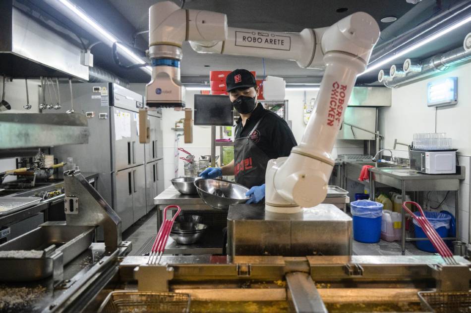 In this photo taken on June 13, 2023, an employee walks past a robot being used to fry chicken, at a Robert Chicken restaurant in Seoul. Anthony Wallace, AFP 